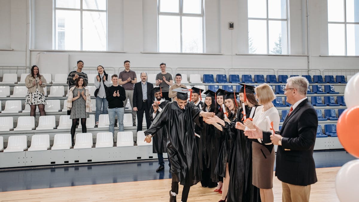 Graduates celebrate their achievement in a gymnasium with friends and family cheering.